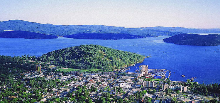 A panoramic aerial view of Lake Coeur d'Alene with many homes, businesses, and the Coeur d'Alene resort in the bottom part of the photo.